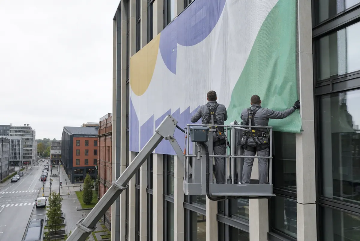 Installers in a boom lift basket fixing a printed mesh banner to an office facade