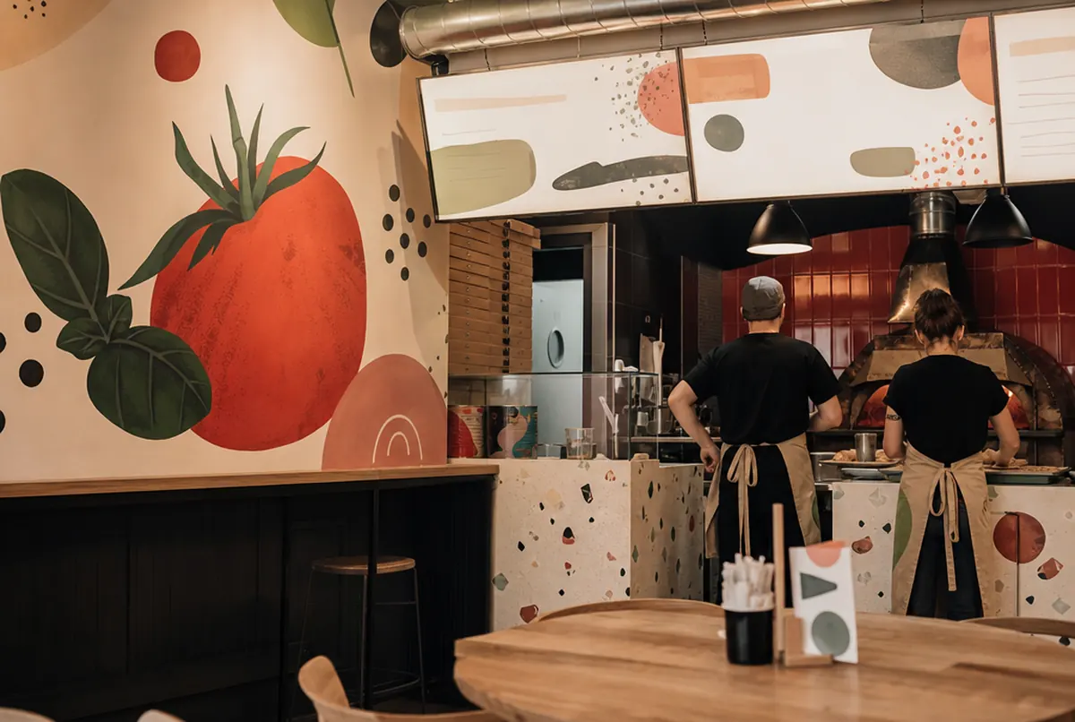 Gastraum einer Pizzeria mit Wandgrafik und Menütafel auf Platte an der Theke
