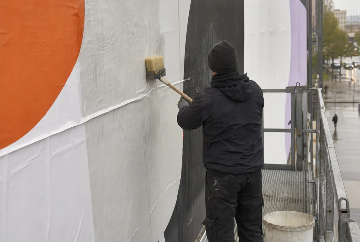 Équipe collant les lés d’une affiche grand format avec une longue brosse