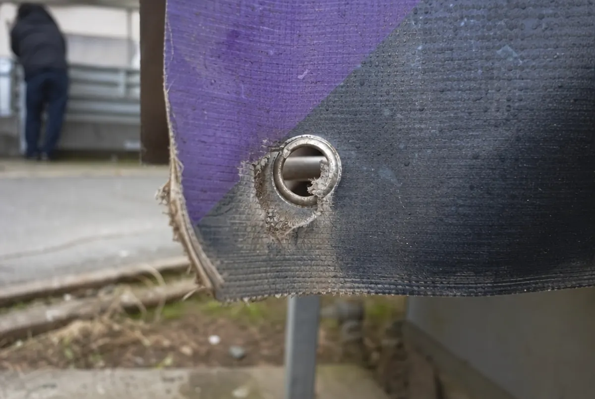 Beschädigter Bannerrand mit ausgerissener Öse und ausgeblichener Farbe