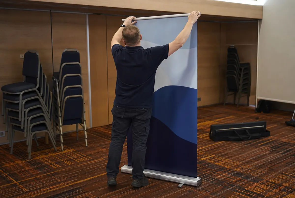 Person rolling a roll-up banner into its cassette in an empty room after an event