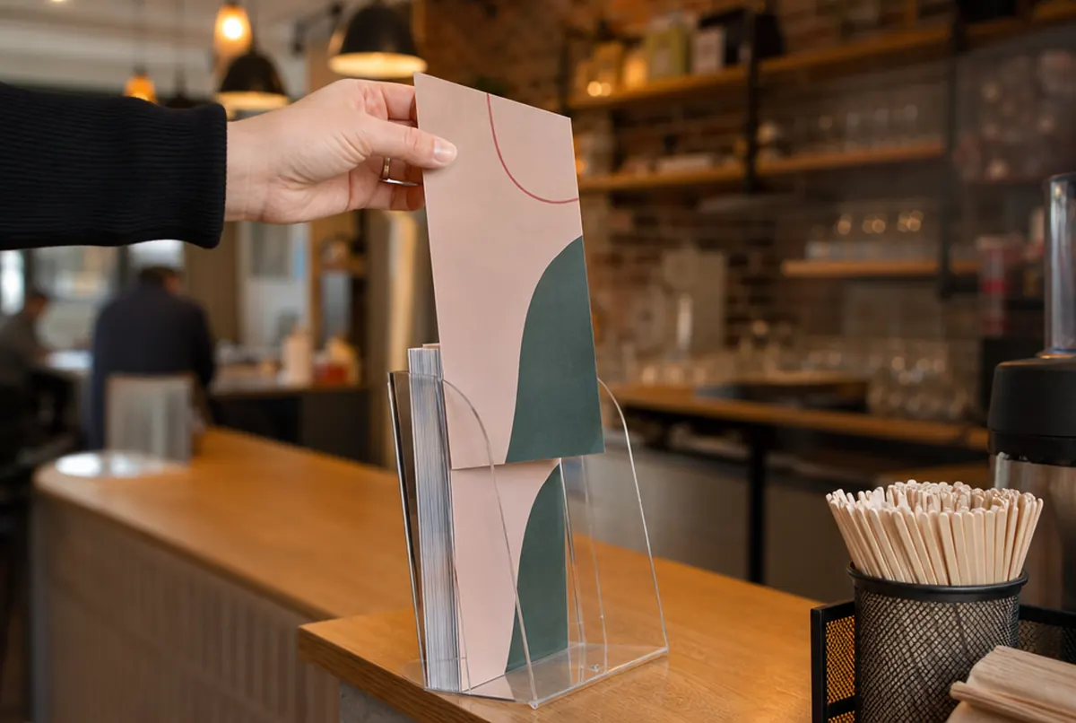 Main prenant un flyer DL dans un présentoir sur le comptoir d’un café