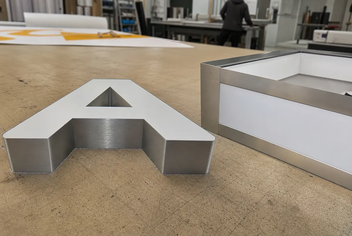 A single built-up letter next to the corner of a light box frame on a workbench