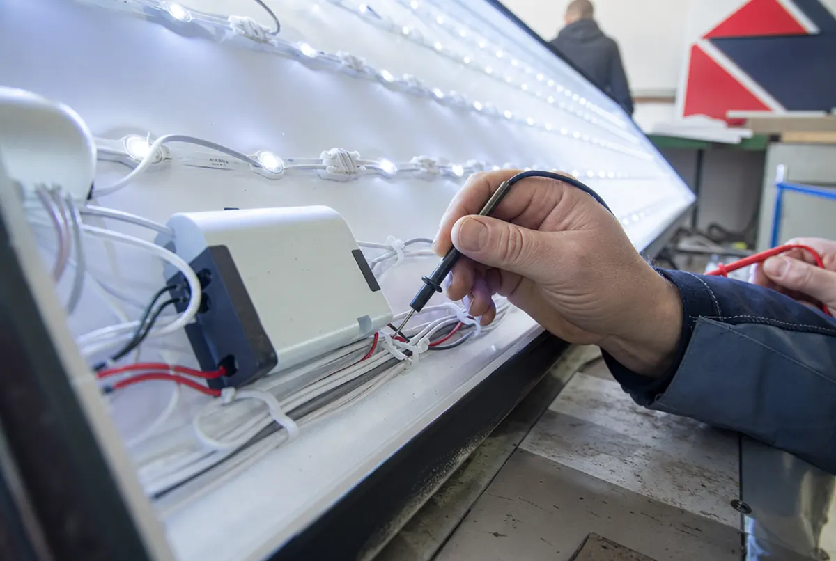 Technicien contrôlant au multimètre les modules LED et l’alimentation d’un caisson
