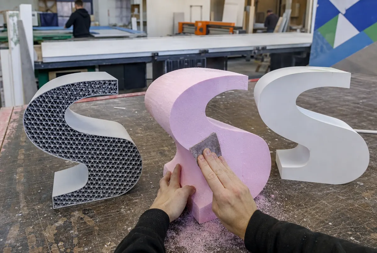 Une lettre imprimée en 3D, une en polystyrène extrudé et une en PVC côte à côte sur une table