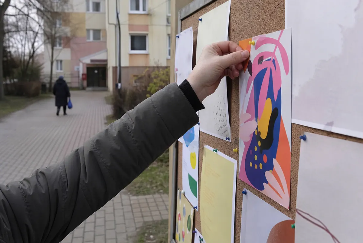 Eine Hand pinnt einen Flyer an ein Schwarzes Brett im Wohngebiet