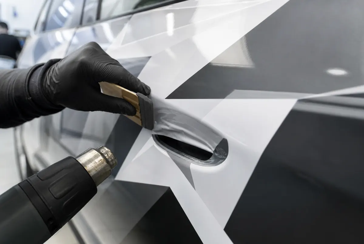 Installer applying vinyl to a car door with a heat gun in a workshop