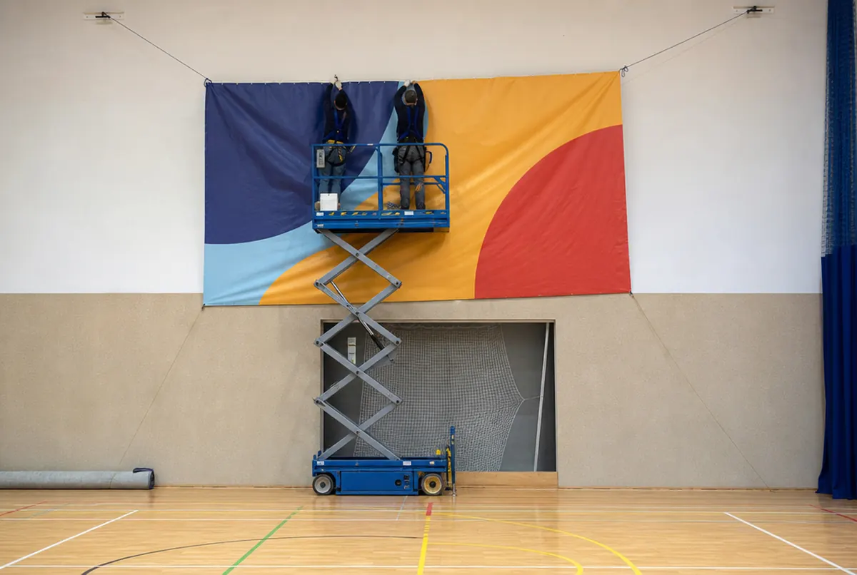 Installers on a lift hanging a banner on a sports hall wall