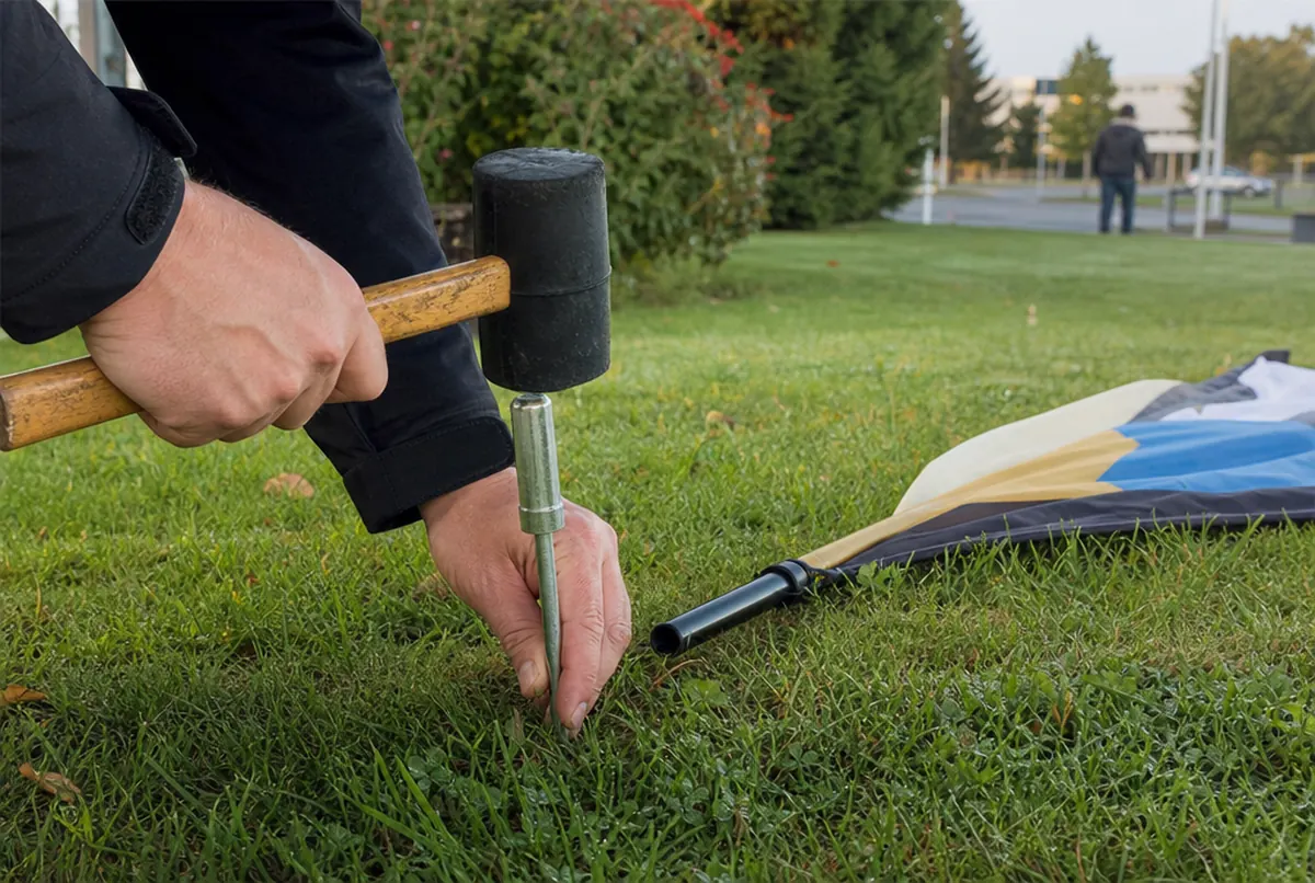 Hands driving a flag ground spike into grass with a mallet