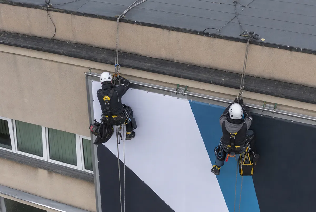 Rope access technicians tensioning a banner on a facade
