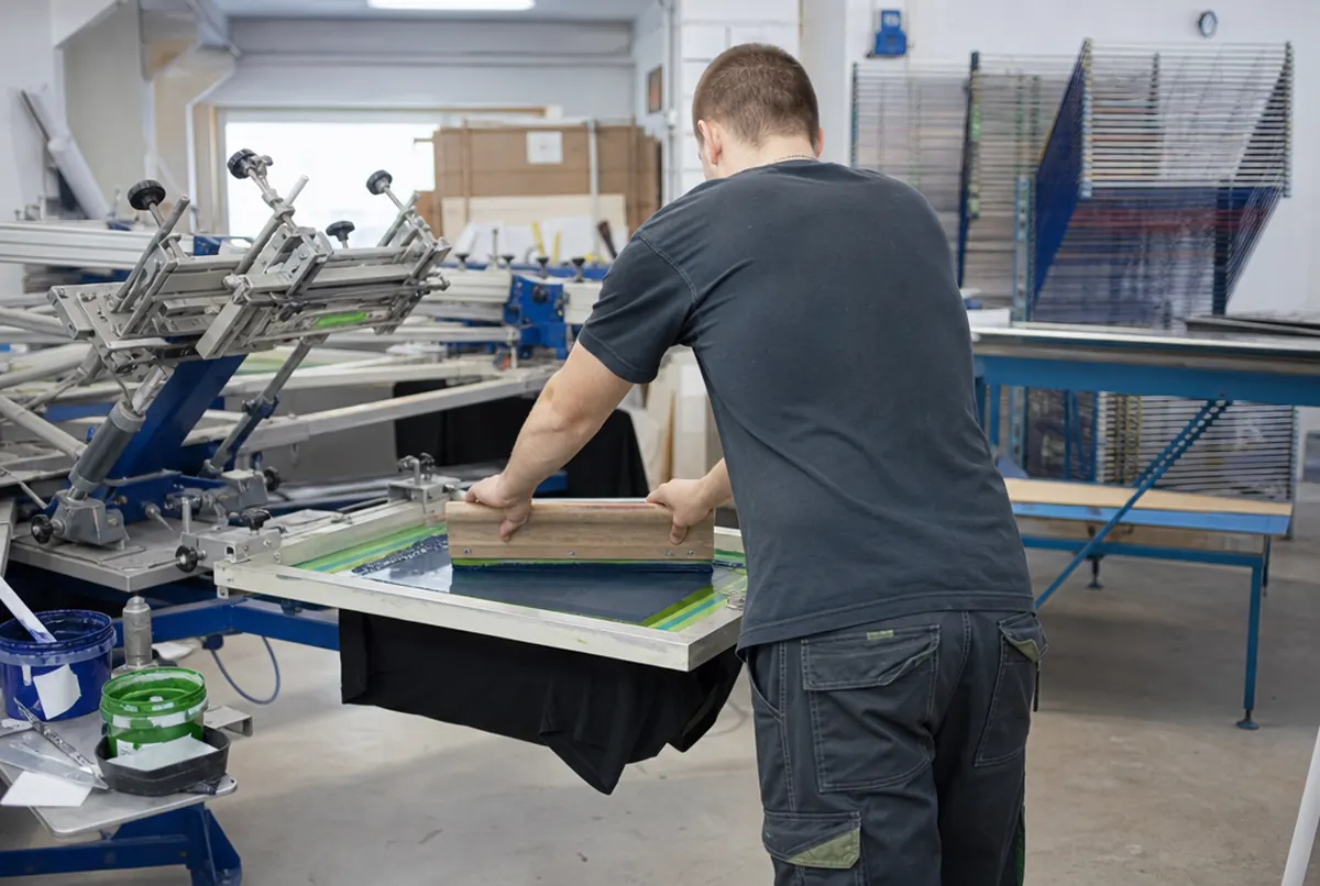 Siebdruck auf T-Shirts: Die Rakel drückt Farbe durch das Sieb