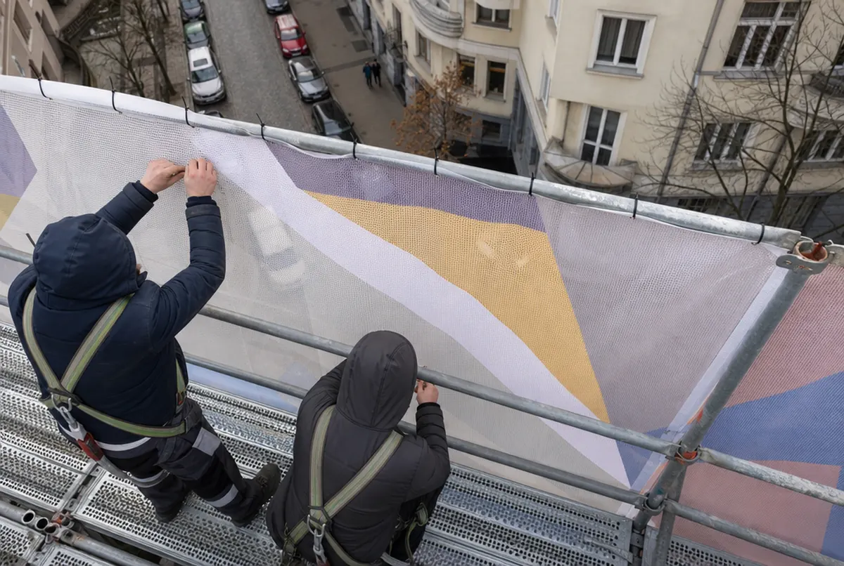 Monteure auf dem Gerüst binden die Kante eines Mesh-Banners fest