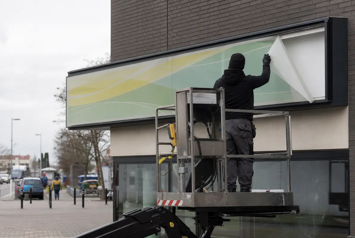 Technician removing the face of a light box above a shop to replace the graphic