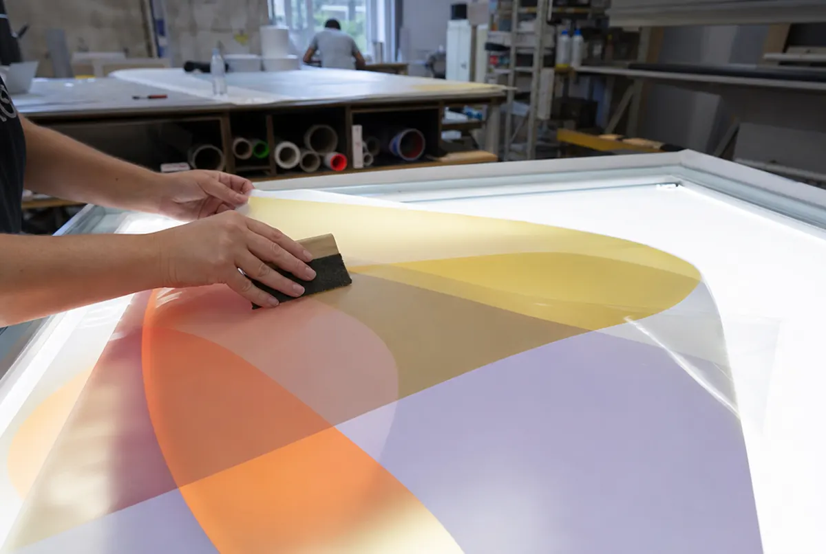 Hands applying backlit film to an acrylic sheet with a squeegee on a table
