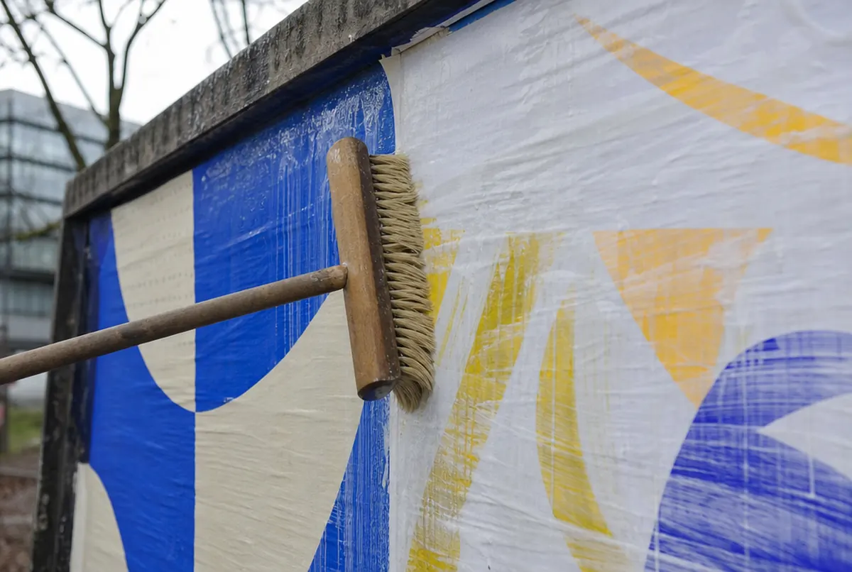 Brush smoothing a fresh blueback poster panel on a billboard, joint between sheets visible