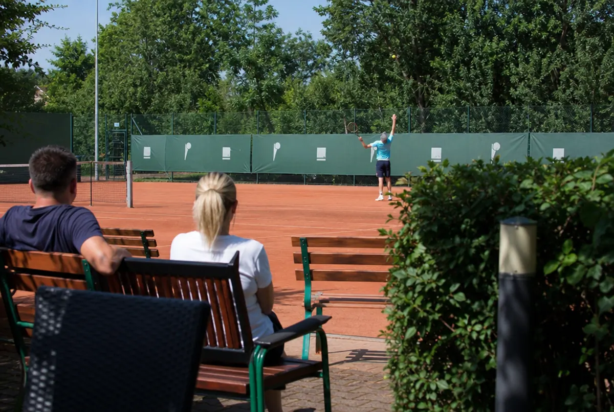 Dark green printed windscreens on the fence of a clay tennis court at a club