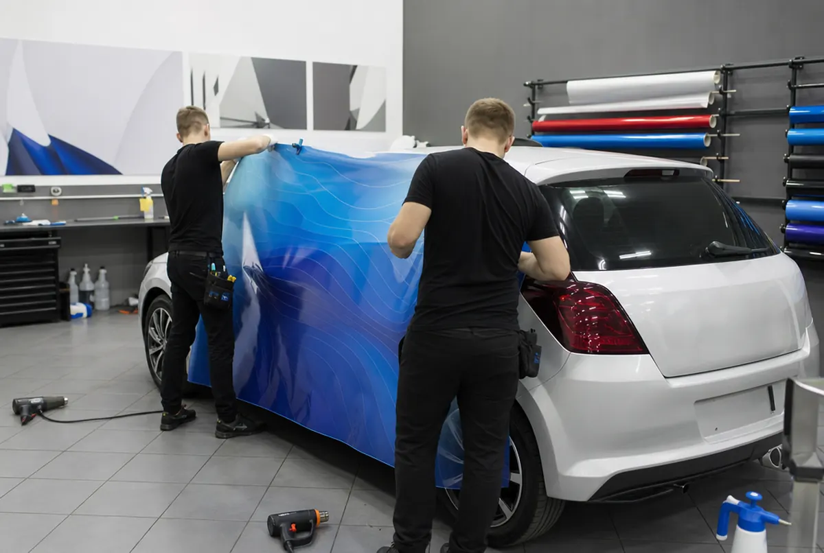 Two installers applying a large cast vinyl panel to the rear of a car in the wrap shop