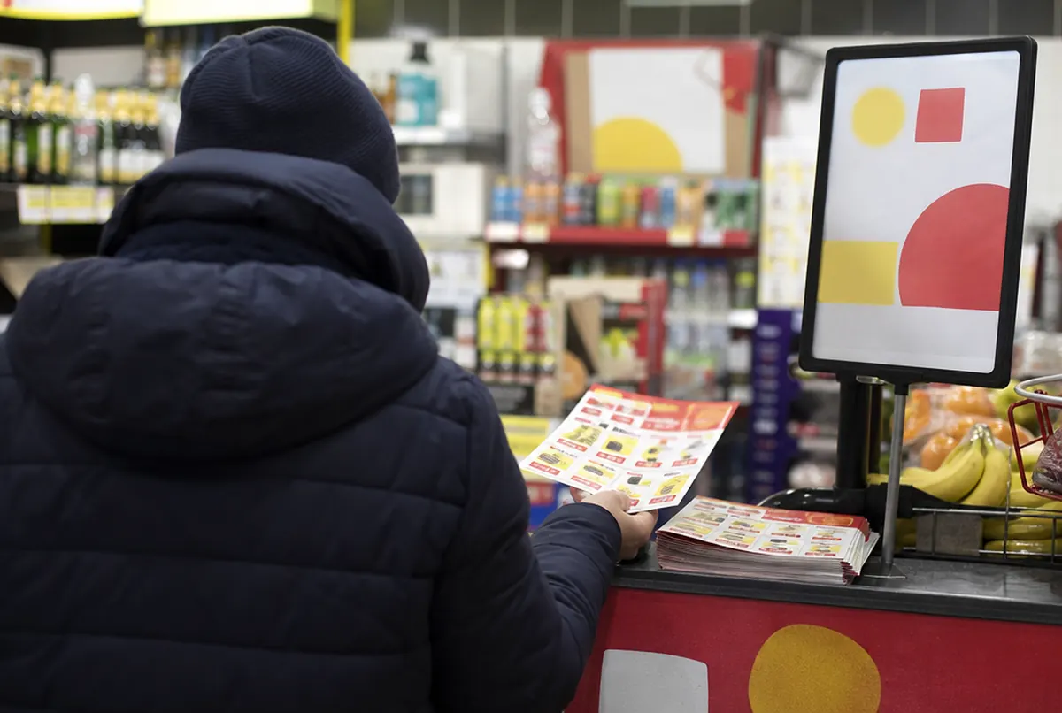 Kundin nimmt ein Prospekt von der Theke an der Kasse eines Lebensmittelladens
