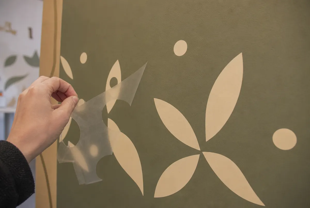 Hand peeling transfer tape off cut vinyl shapes on a painted wall