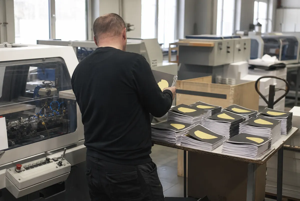 Brochures piquées à cheval sortant de la machine en atelier de façonnage