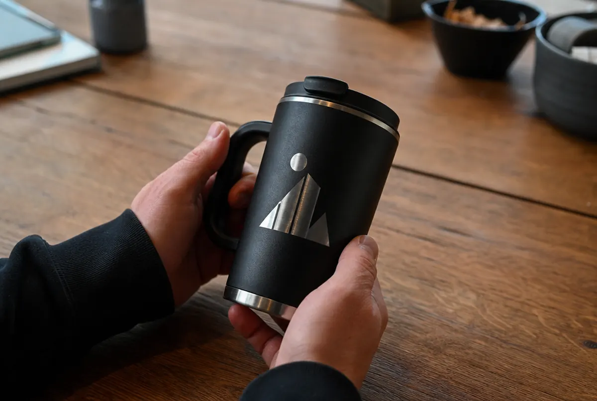 Close-up of a laser engraving on a black stainless steel thermal mug held in hands
