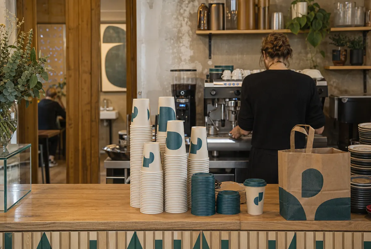 Gobelets à emporter imprimés sur le comptoir d'un café, barista en arrière-plan