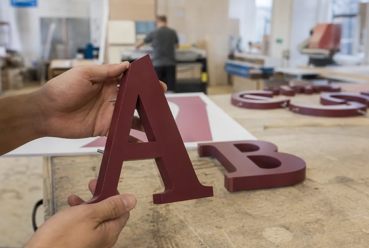 Hands holding a burgundy 3D PVC letter with a clean milled edge and mounting pins