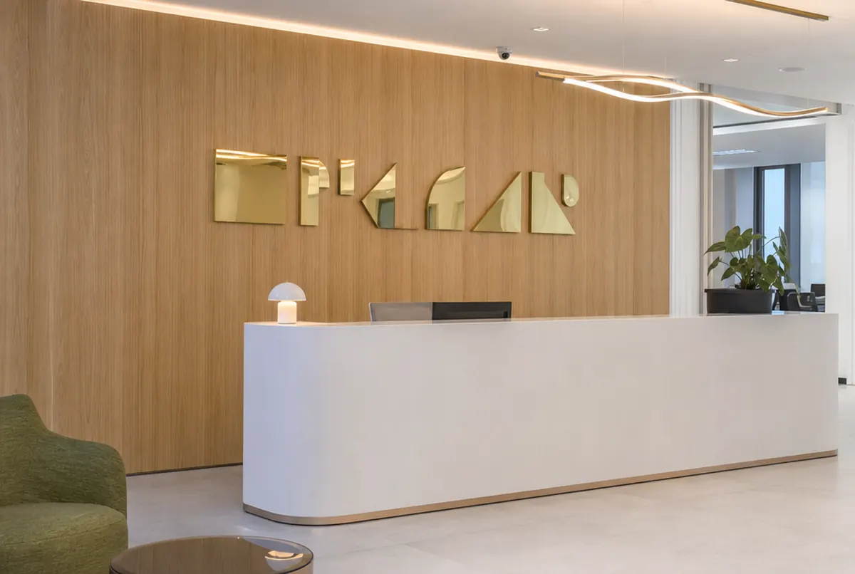 Gold mirror-finish 3D logo letters on an oak wall behind an office reception desk