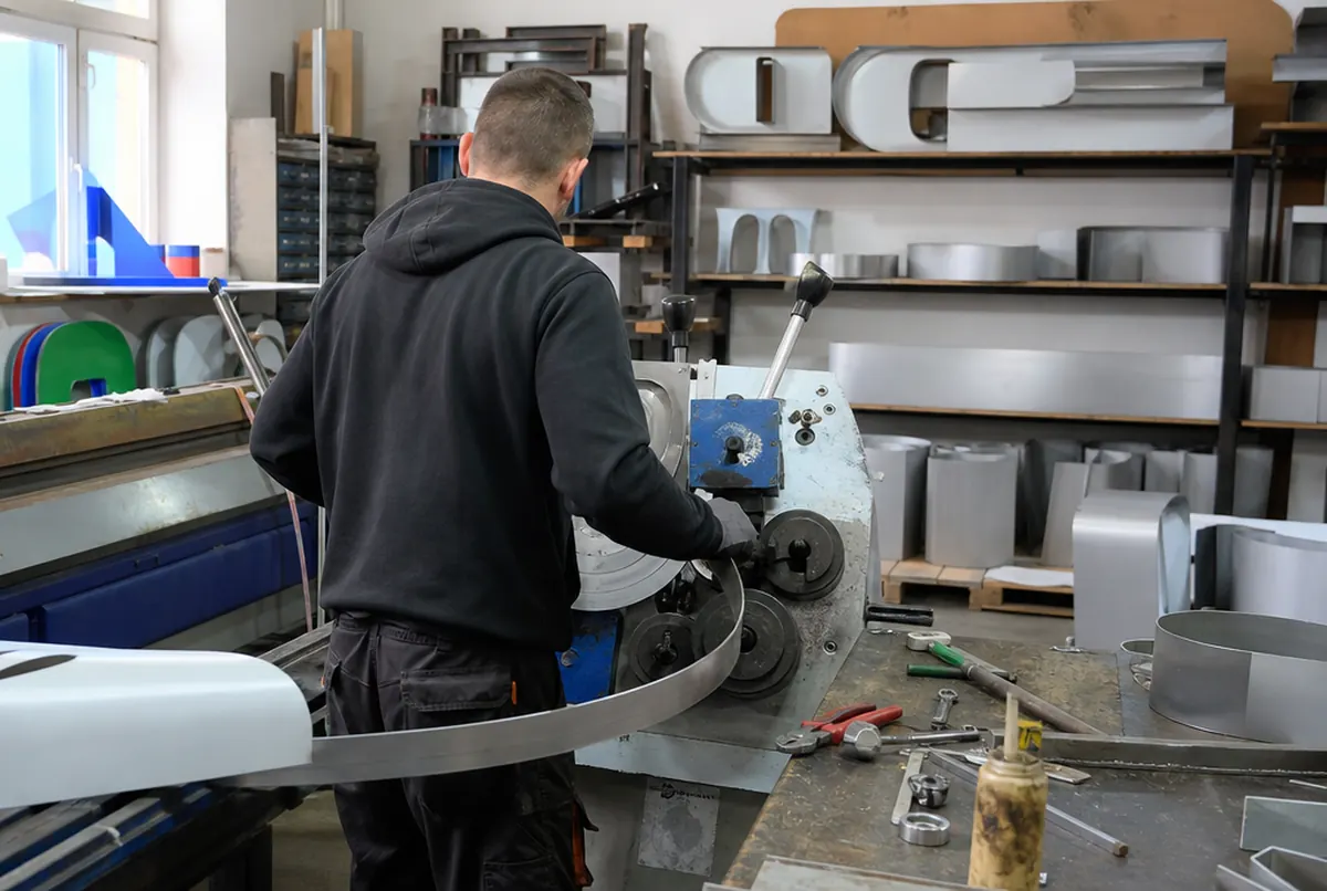 Un técnico da forma al canto de aluminio de una letra corpórea