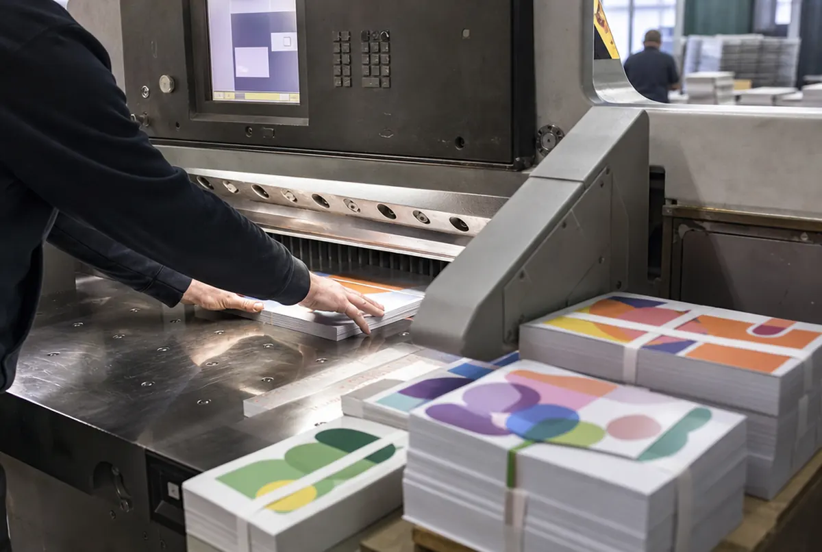 Guillotine trimming a stack of sticker sheets to size, finished bundles nearby