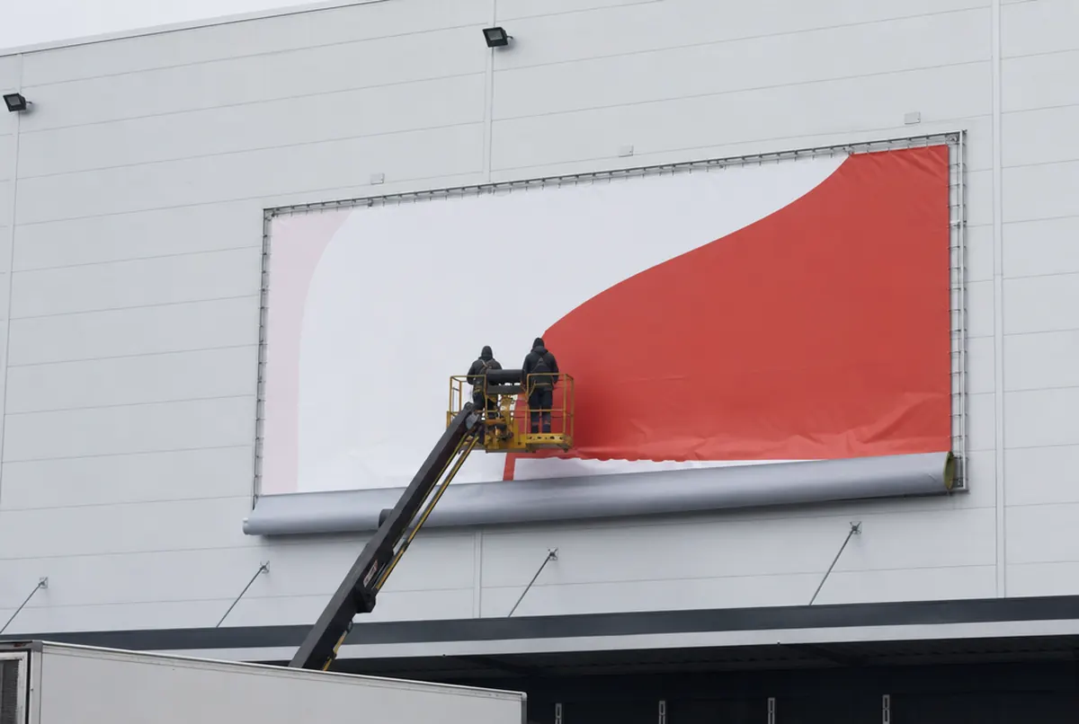 Installers on a lift replacing the banner in an existing frame on a warehouse wall