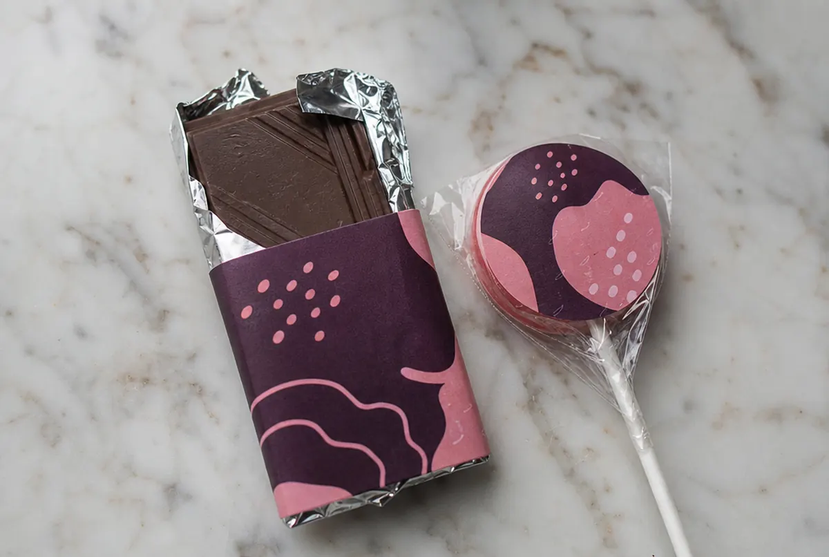 Close-up of a mini chocolate bar with a printed band and a lollipop with a sticker