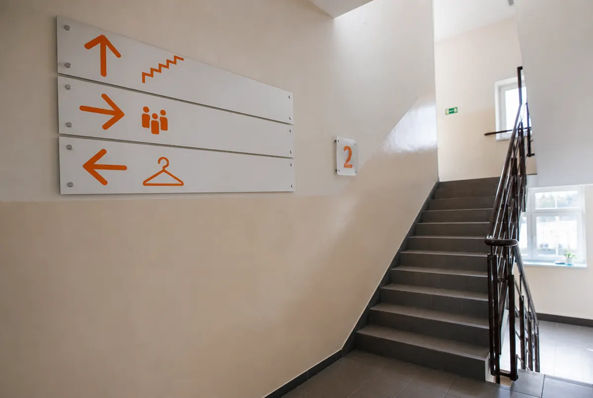 Orangefarbene Richtungspfeile und Etagenschild im Treppenhaus einer Schule