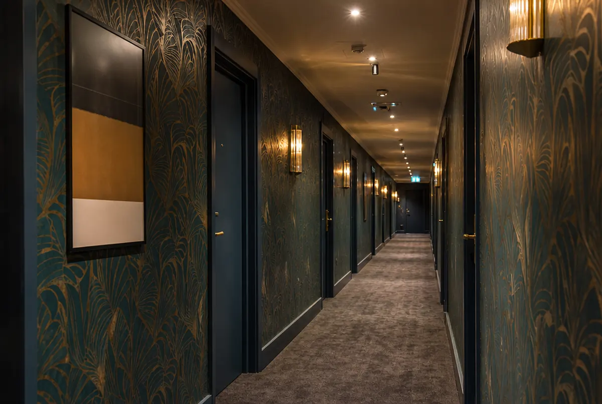 Couloir d'hôtel tapissé d'un motif botanique répété bleu canard et or