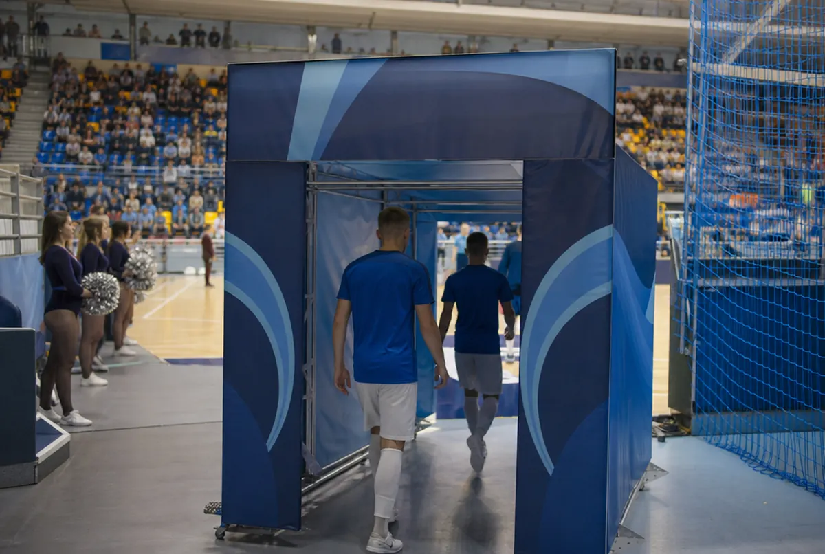 Team walking out onto the court through a printed player tunnel in a sports hall