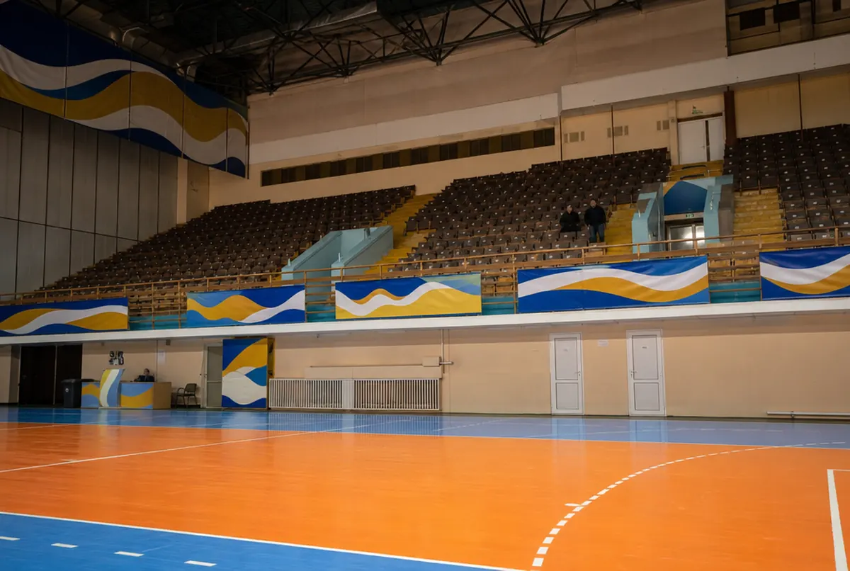 Sporthalle von Spielfeldhöhe: Banner mit blau-gelb-weißen Wellen an den Tribünengeländern und orangefarbener Boden