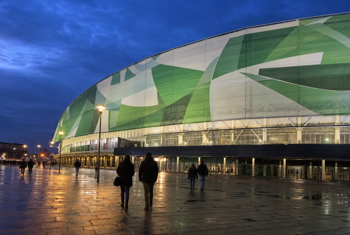 Sporthalle am Abend: beleuchtete Fassade mit großem grün-weißem geometrischem Banner über einem nassen Platz
