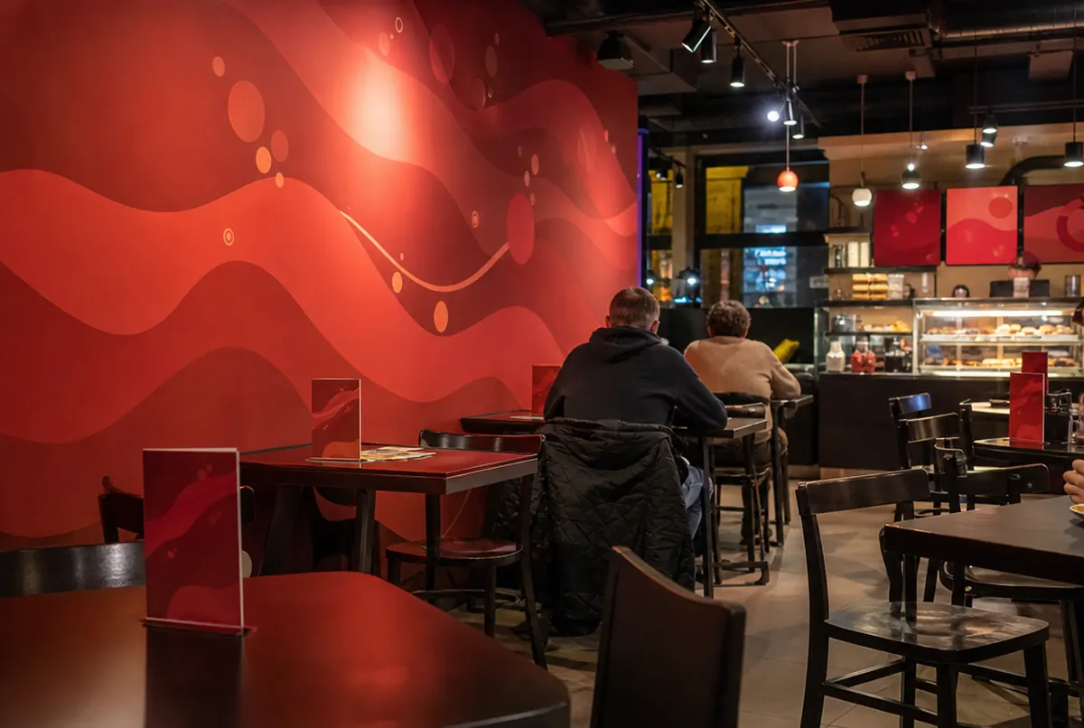 Café am Abend: rotes Wandbild mit Wellen und Blasen und rote Tischaufsteller auf dunklen Tischen