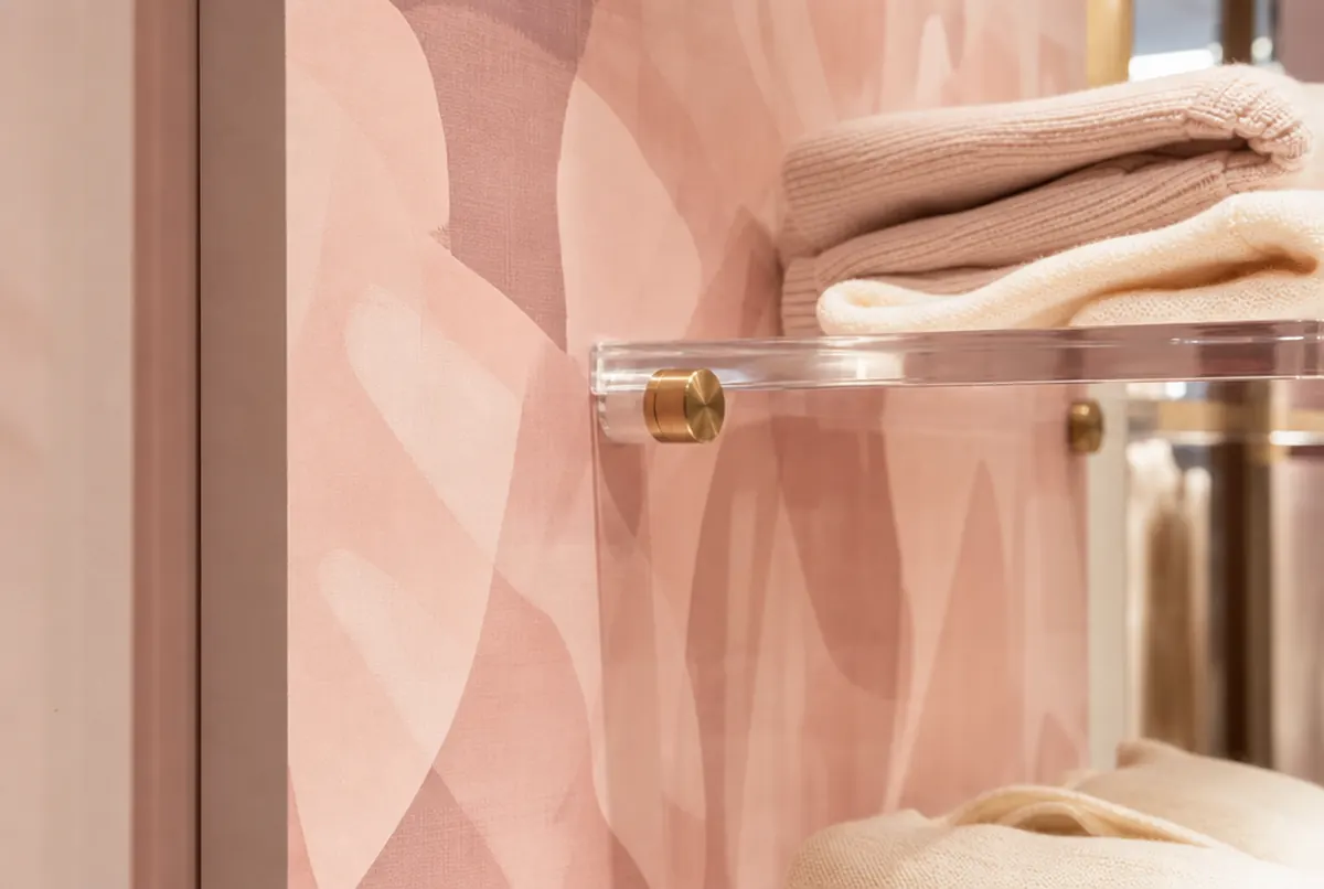 Detail im Laden: puderrosa Wandpaneel mit dezentem Muster und eine Acrylablage mit gefalteten Strickteilen